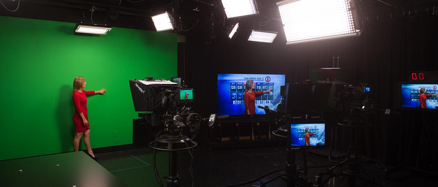 Broadcaster in red dress in studio performing a meteorology broadcast